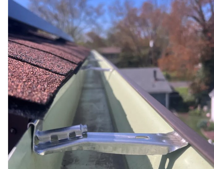 Gutter cleaning scoop clearing debris from a roof edge gutter