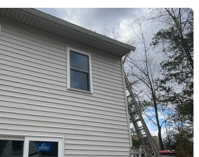 Ladder set against gray siding during a gutter installation
